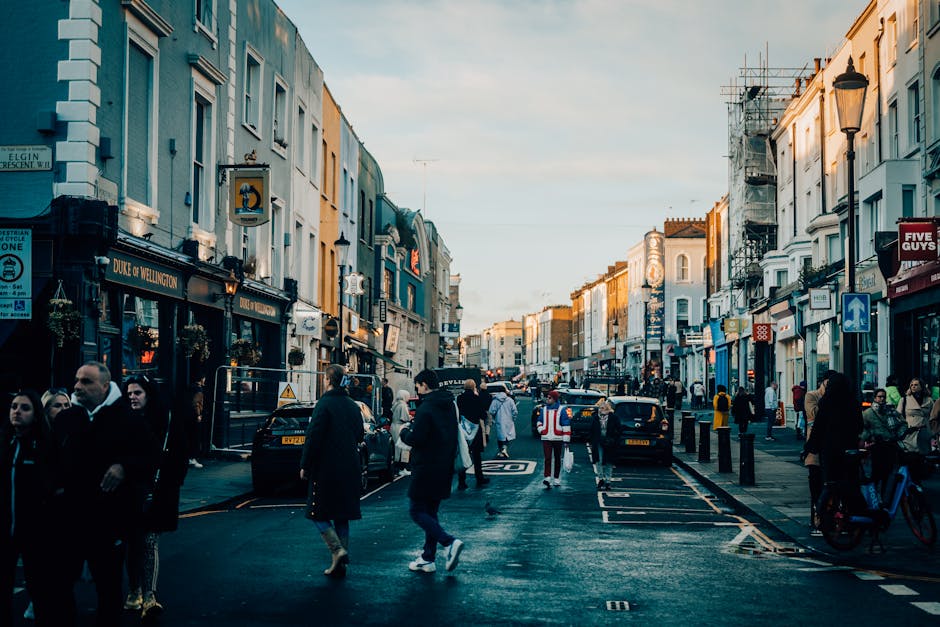The image depicts a busy street scene in Westminster, London, with the buildings on either side featuring a mix of modern and historic architectural styles. The street is lined with shops, cafes, and 